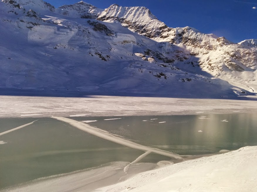 Montagne innevate, uno specchio d'acqua ghiacciato e il cielo blu. Spettacolo naturale suggestivo che si apre davanti agli occhi di chi percorre il tragitto da Tirano a Saint-Moritz nel periodo invernale